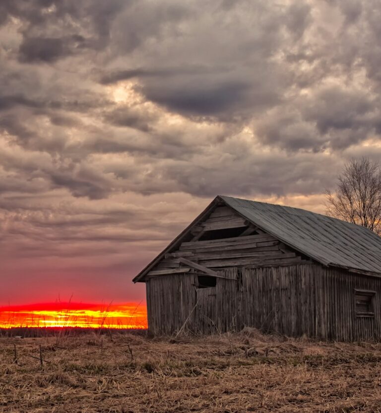 Weathered wooden barn under a stormy sunset sky